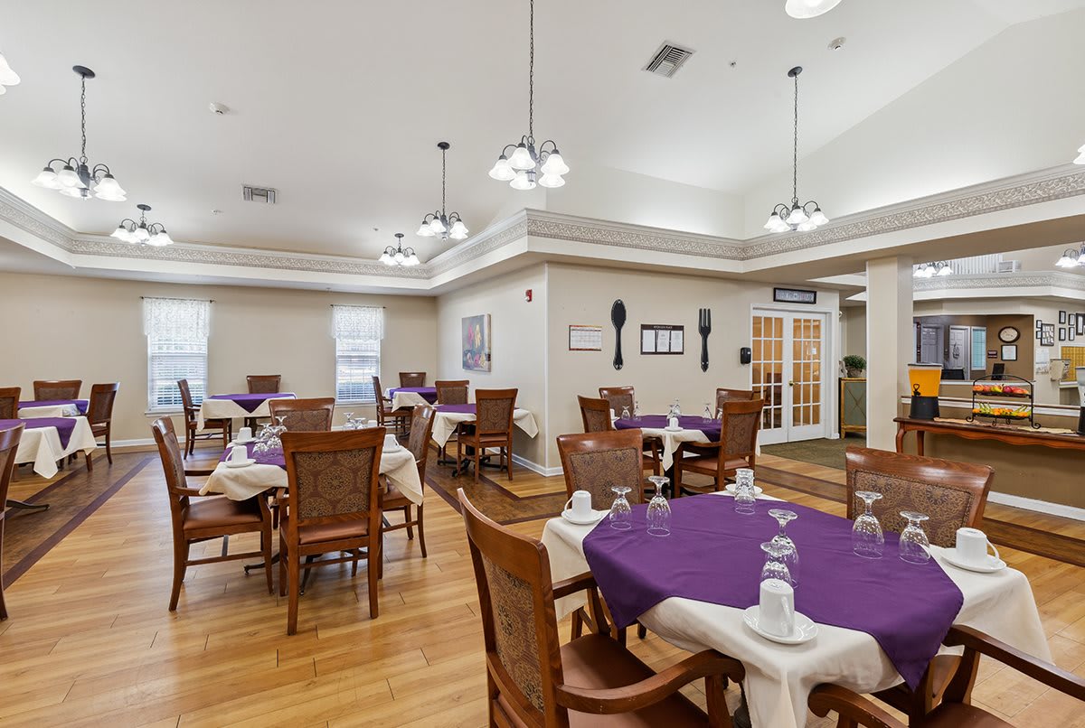 A well-lit dining room with neatly arranged tables and chairs, featuring a wooden floor and elegant lighting.