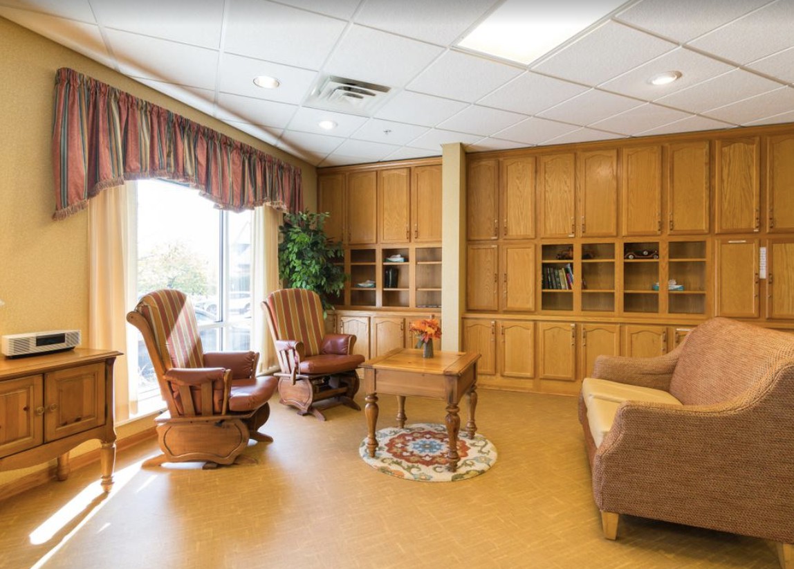 A cozy living room with rocking chairs, wooden shelves, and sunlight streaming through large windows.