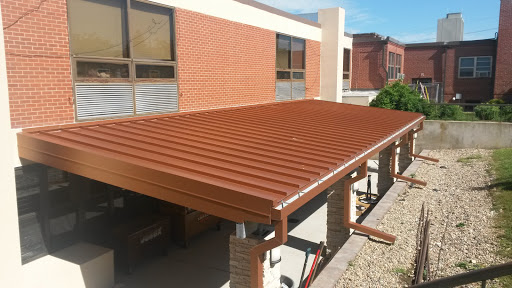 A newly constructed metal roof over a patio area adjacent to a building.