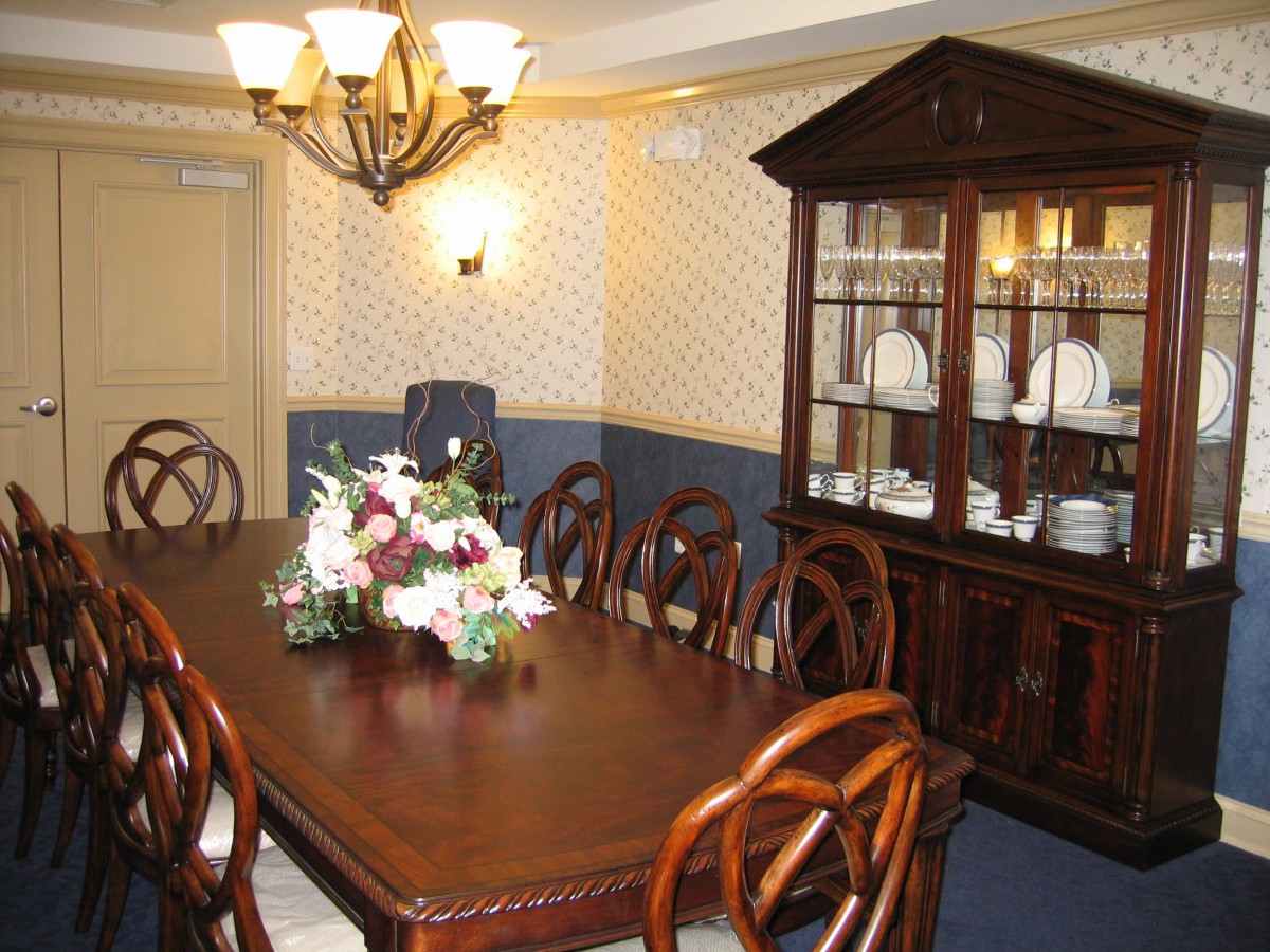 A dining room with a wooden table, chairs, and a cabinet, elegantly decorated with a floral centerpiece and chandelier.