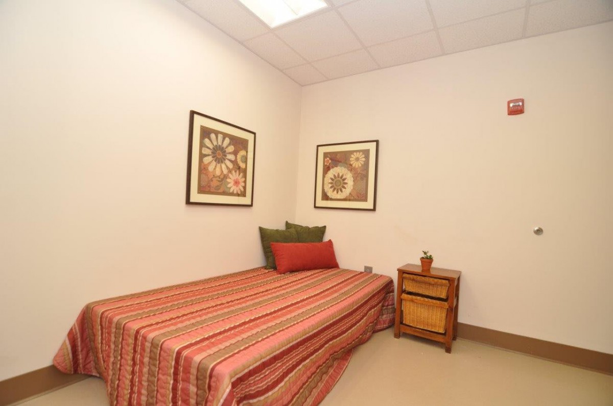 A simple and minimalist bedroom with a single bed, striped bedding, decorative pillows, a small wooden nightstand, and two floral-themed artworks on the walls.