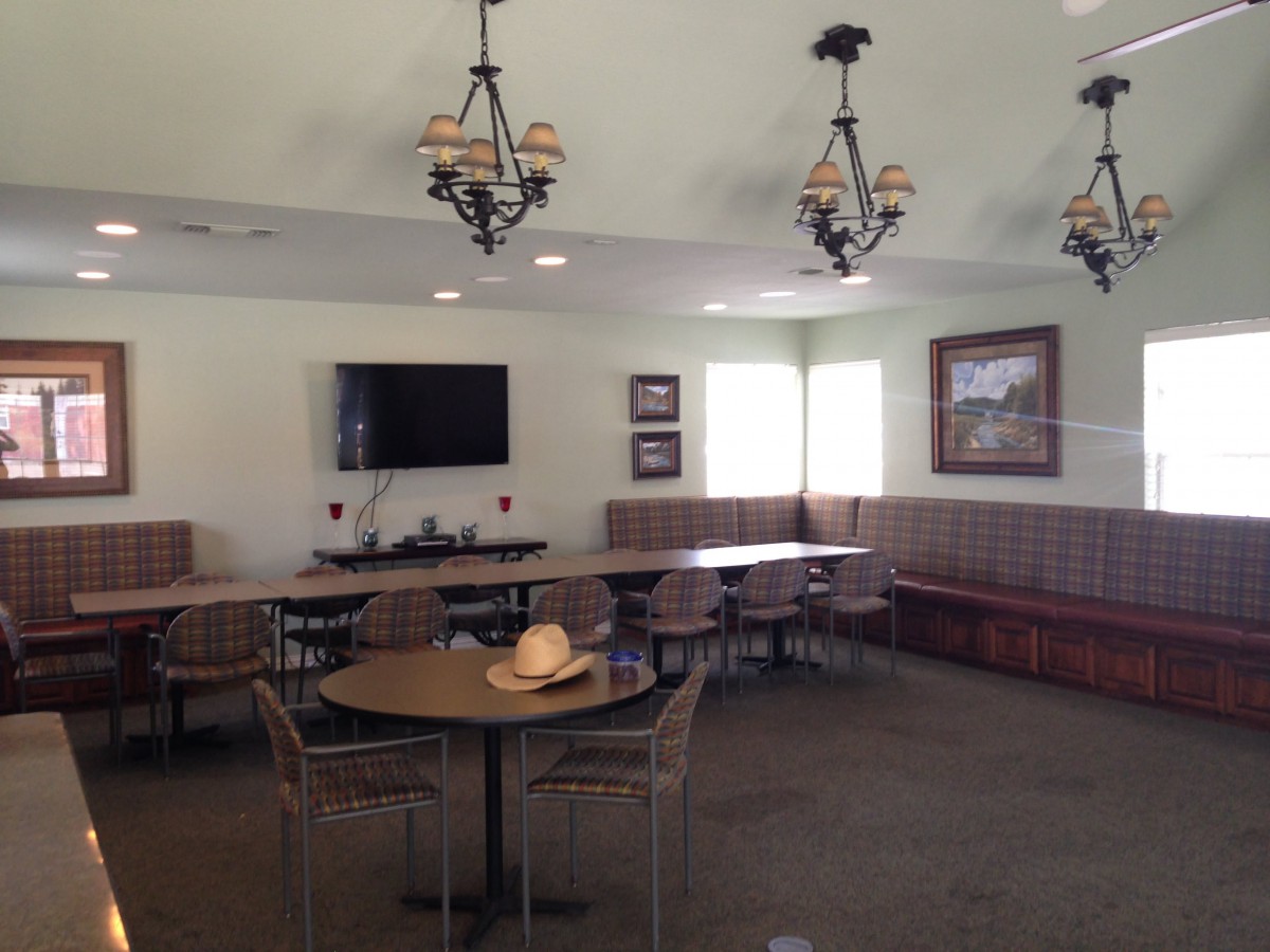 A cozy dining area with tables, chairs, chandeliers, and a hat on a table.