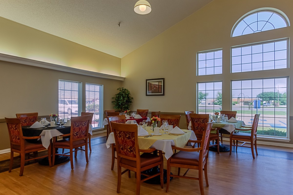 A well-lit dining area with neatly arranged tables and chairs, featuring large windows and elegant decor.