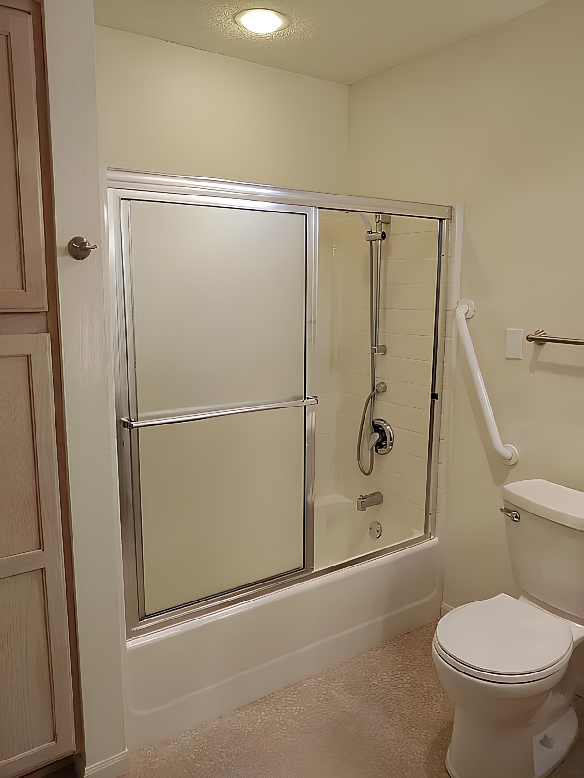 A bathroom with a bathtub and shower enclosure featuring sliding glass doors, alongside a toilet and grab bar for safety.