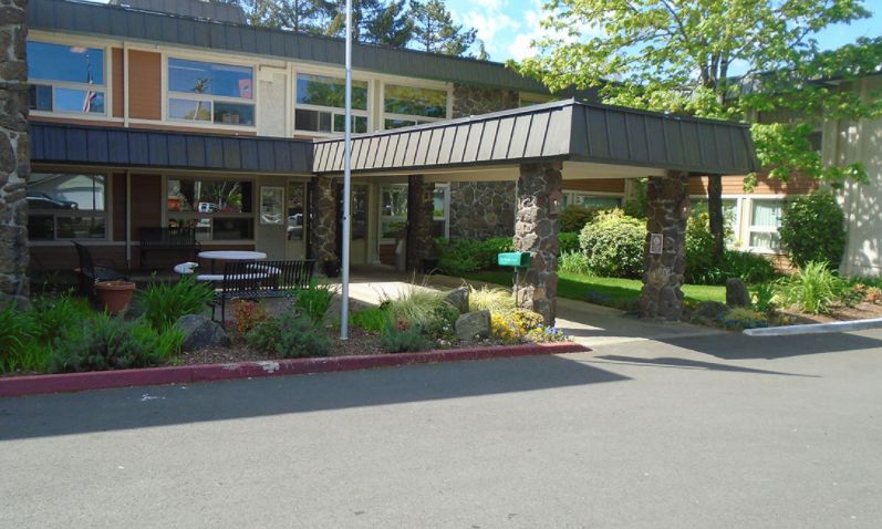 Exterior view of a building entrance with landscaping and a flagpole on a sunny day.
