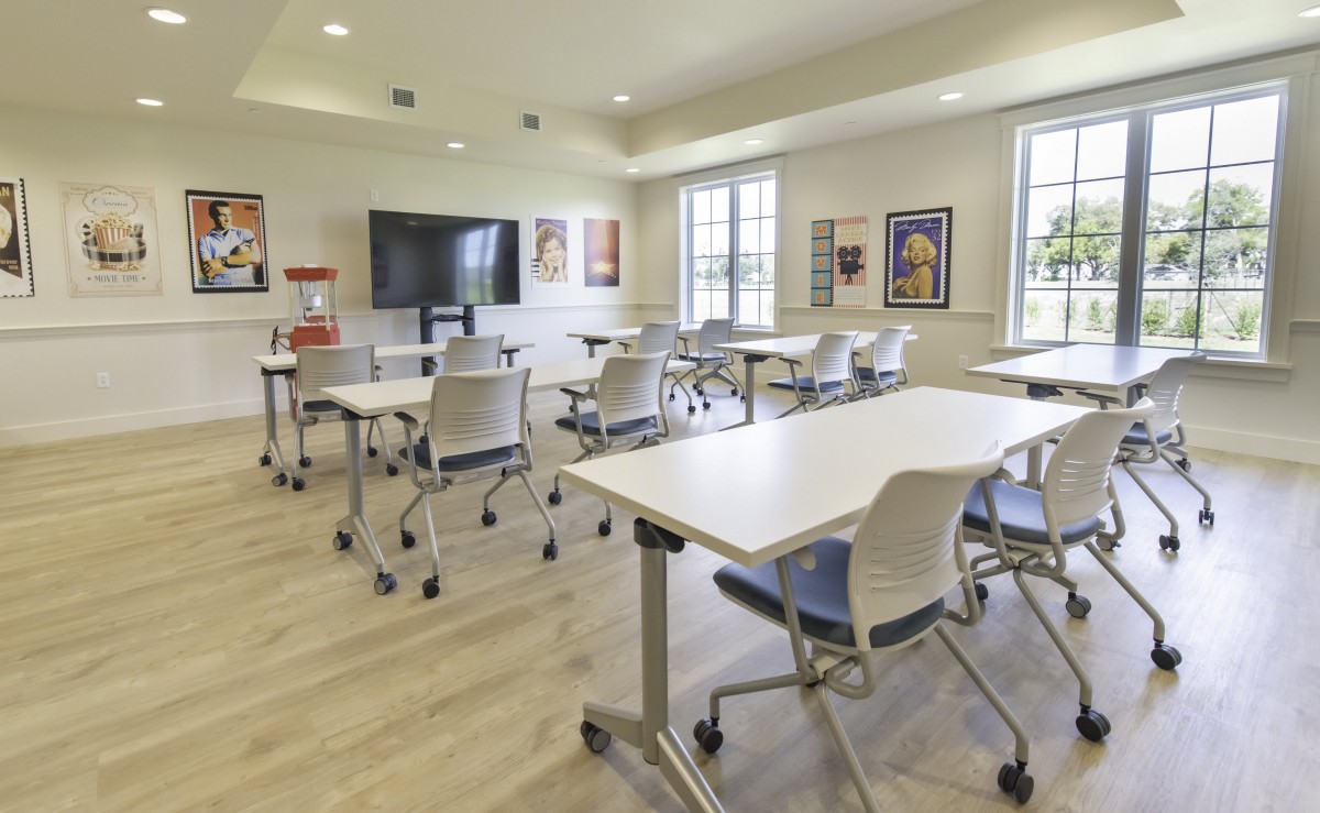 A modern classroom with neatly arranged desks and chairs, featuring a large screen and windows that let in natural light.