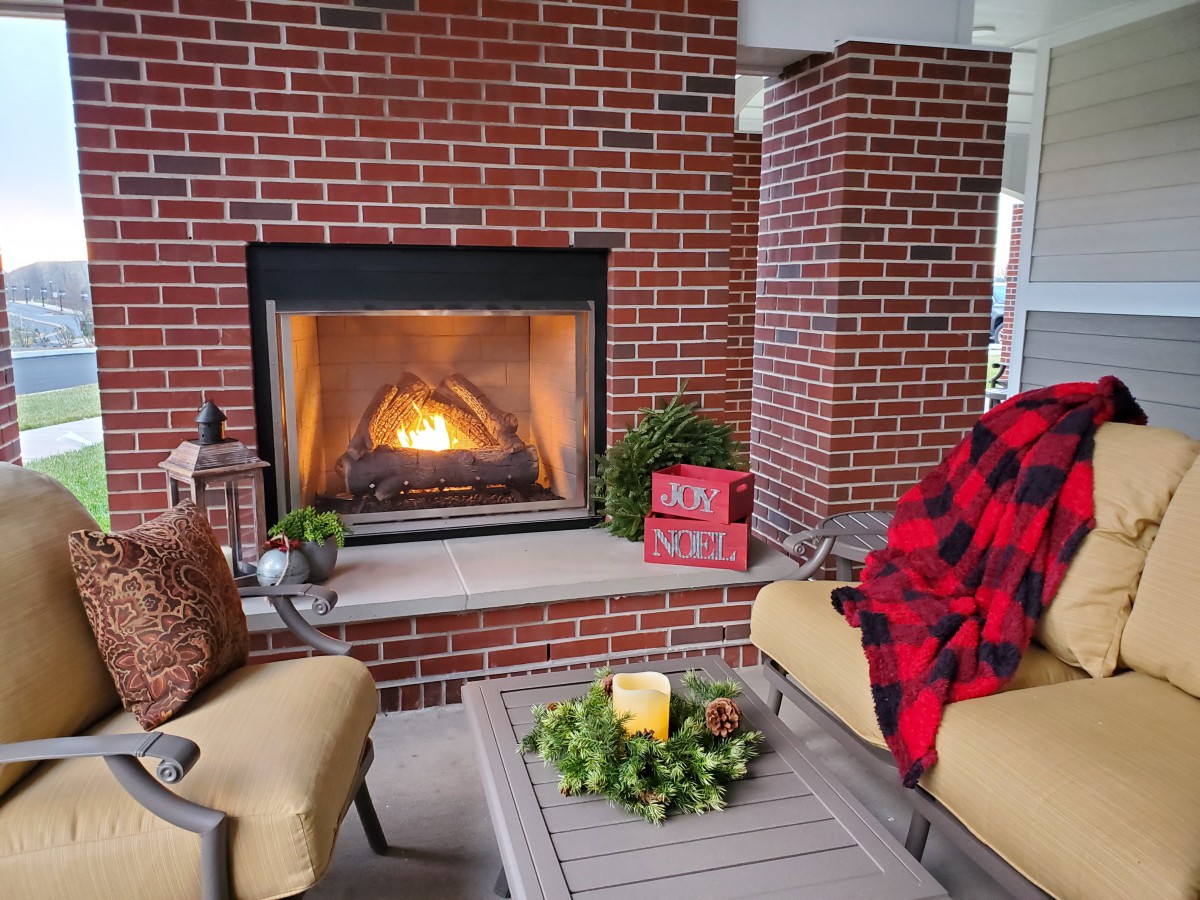 A cozy outdoor seating area with a brick fireplace, comfortable chairs, and a warm blanket.