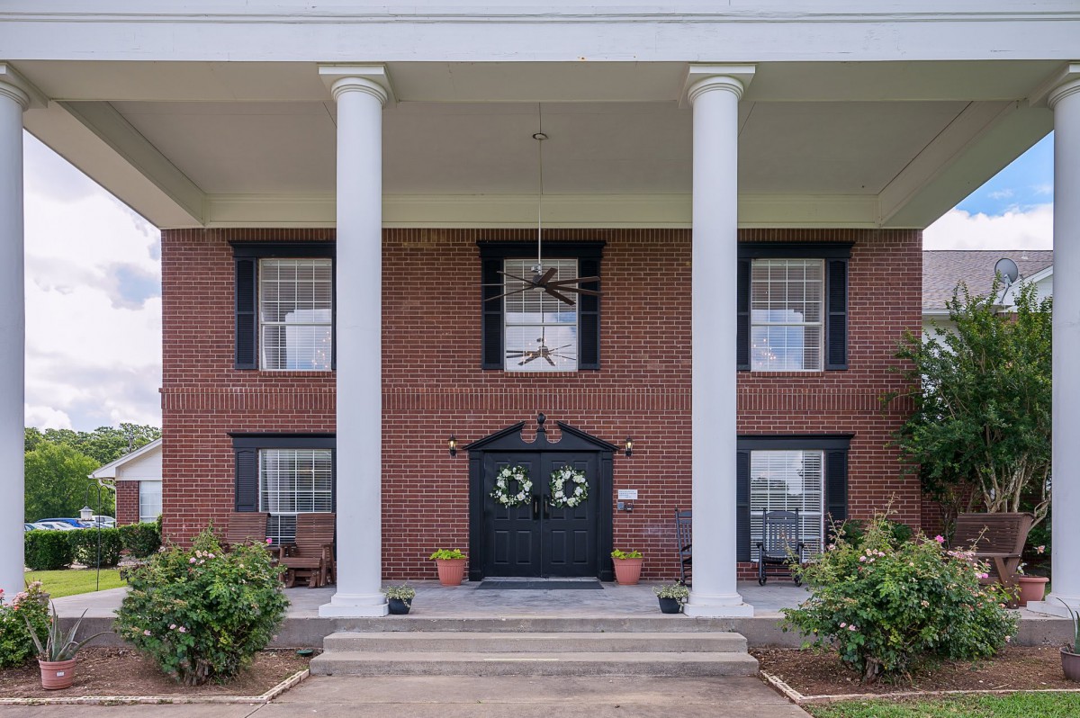 A colonial-style brick house with prominent white columns and a welcoming front entrance adorned with decorative wreaths.
