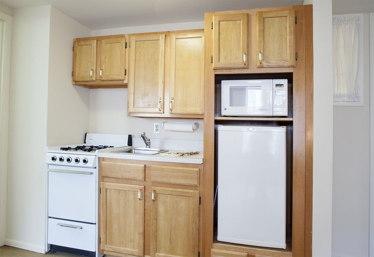A compact kitchen with wooden cabinets, a stove, microwave, and refrigerator.