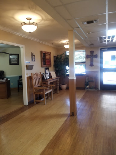 A cozy waiting area featuring wooden floors and chairs, with decor including plants and a cross.