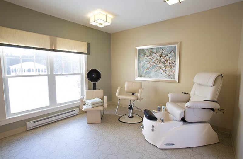 A modern spa salon room featuring a pedicure chair, contemporary artwork, and ample natural light.