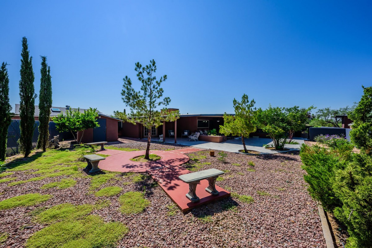 A landscaped garden with benches, trees, and a paved pathway under a clear blue sky.