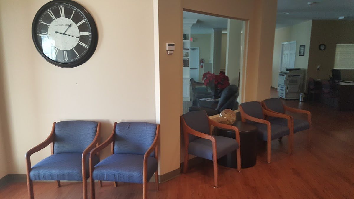 An office waiting area with blue chairs and a wall clock.