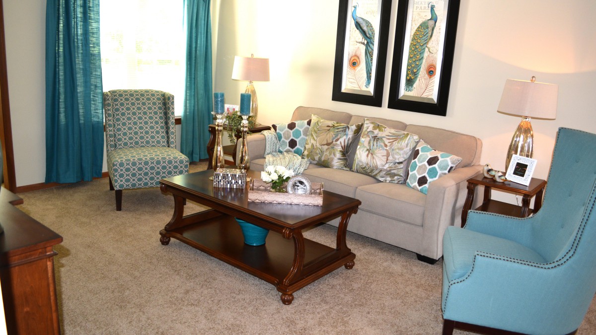 A cozy living room with a beige sofa, patterned armchairs, a wooden coffee table, and decorative artwork on the walls.