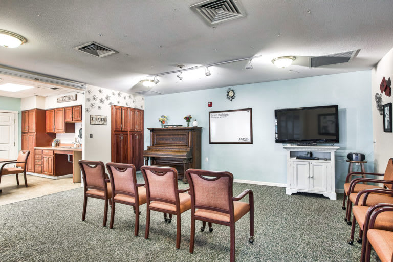 A cozy room with chairs facing a piano and a television, providing a space for gatherings or entertainment.