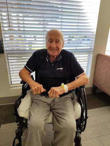 An elderly man with a warm smile sitting in a wheelchair indoors.