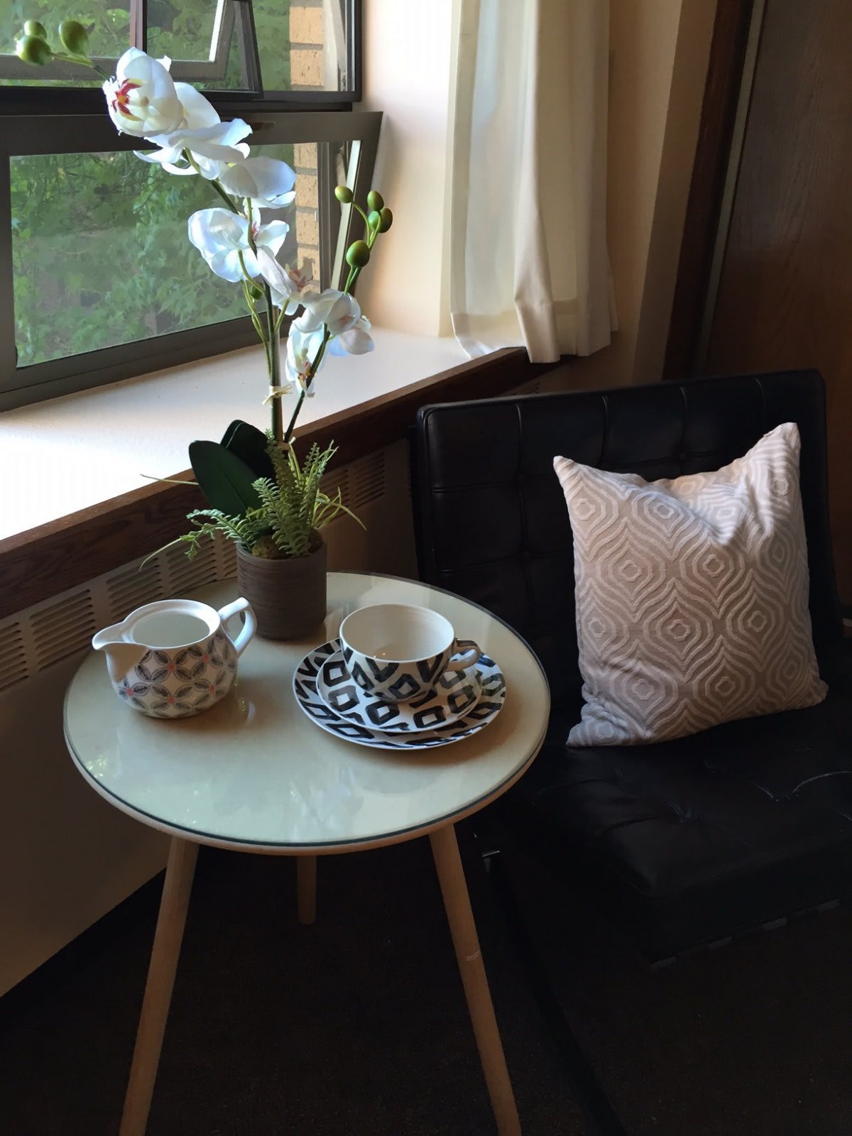 A cozy corner with a small table set for tea, accompanied by a potted plant and cushioned chair beside the window.