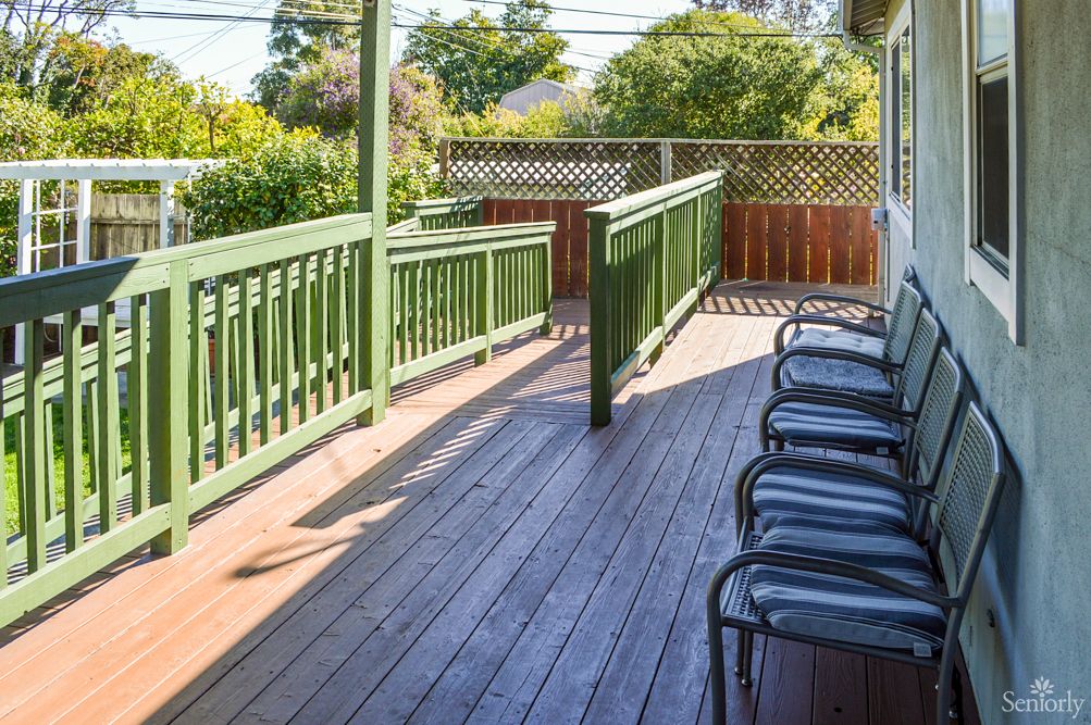 A wooden deck with a ramp, chairs, and surrounding garden.