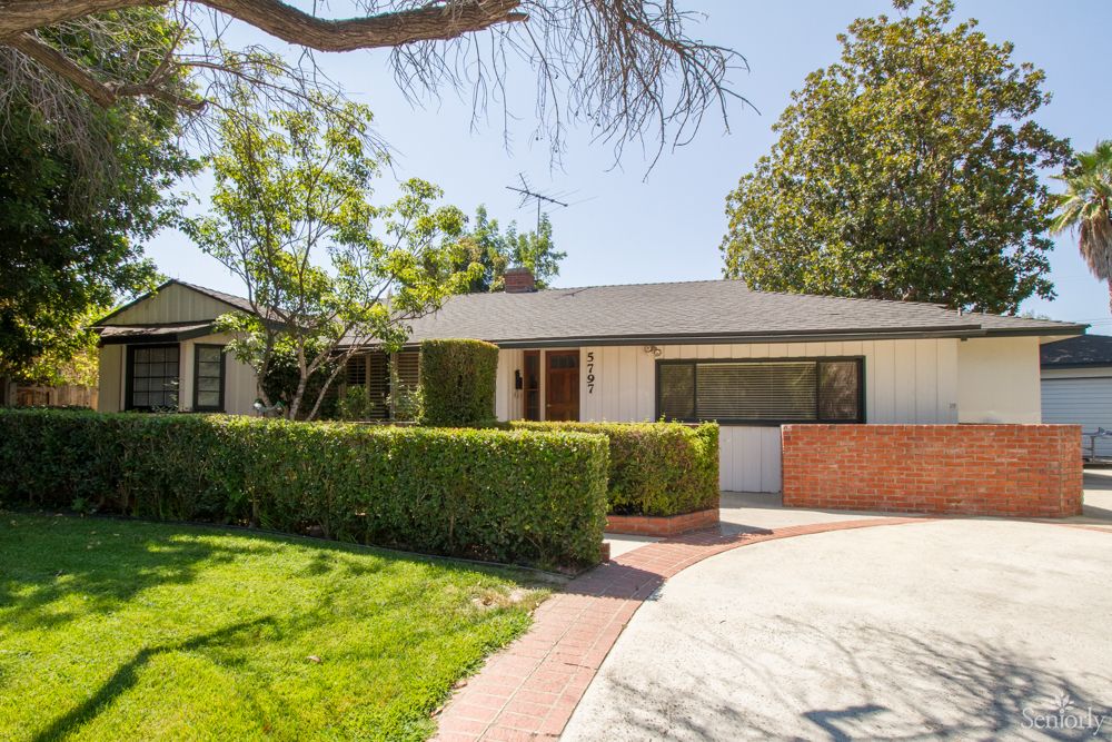 A charming residential house with a well-maintained front yard and a circular driveway under a sunny sky.