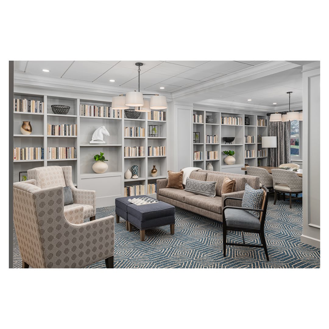 A cozy library interior featuring bookshelves, a sofa, armchairs, and a coffee table.