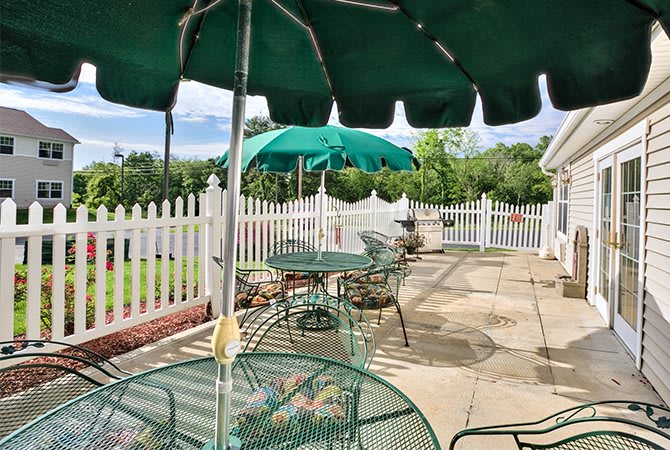 A sunny patio with green umbrellas and metal furniture, surrounded by a white picket fence.