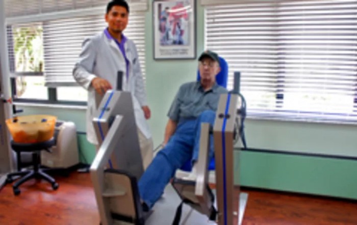 A medical professional assists a patient using exercise equipment for rehabilitation.