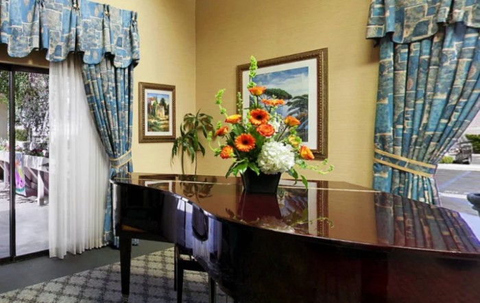 A beautifully decorated room featuring a grand piano with a floral arrangement on top, surrounded by artwork and elegant curtains.