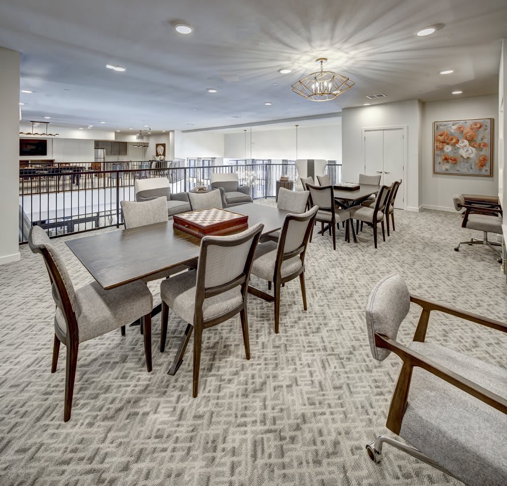 A modern interior living space with tables and chairs, featuring a well-lit environment and carpeted flooring.