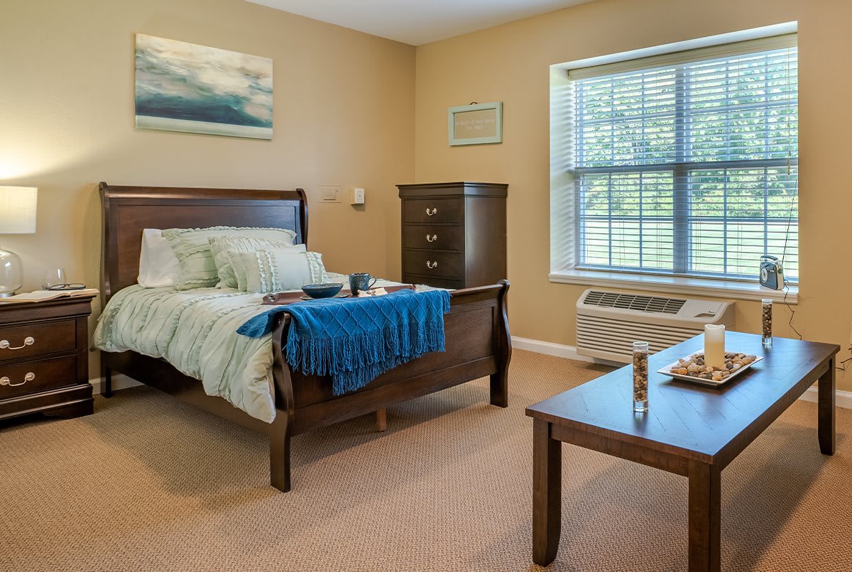 A cozy bedroom interior with a bed, dresser, and large window.