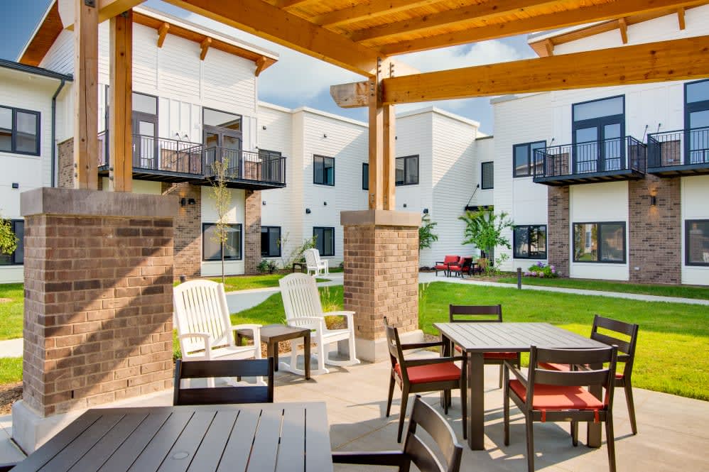 A modern apartment complex with an inviting outdoor patio area featuring tables and chairs in a landscaped courtyard.