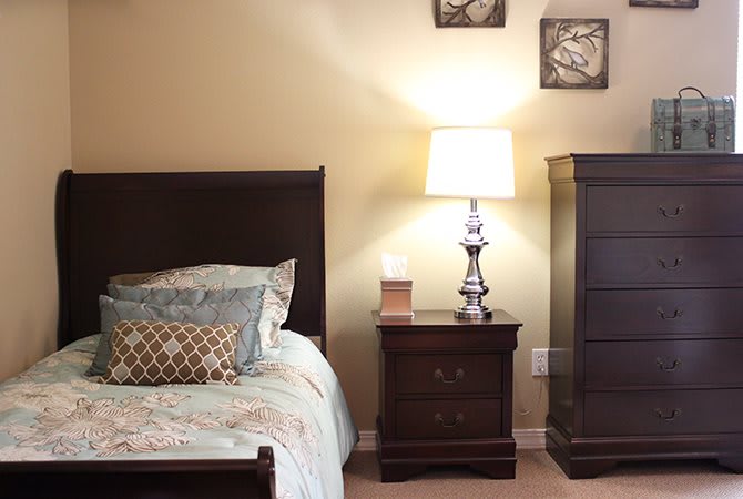 A cozy bedroom with a neatly made bed, nightstand, and lamp.