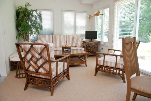 A cozy living room with rattan furniture, a television, and large windows.