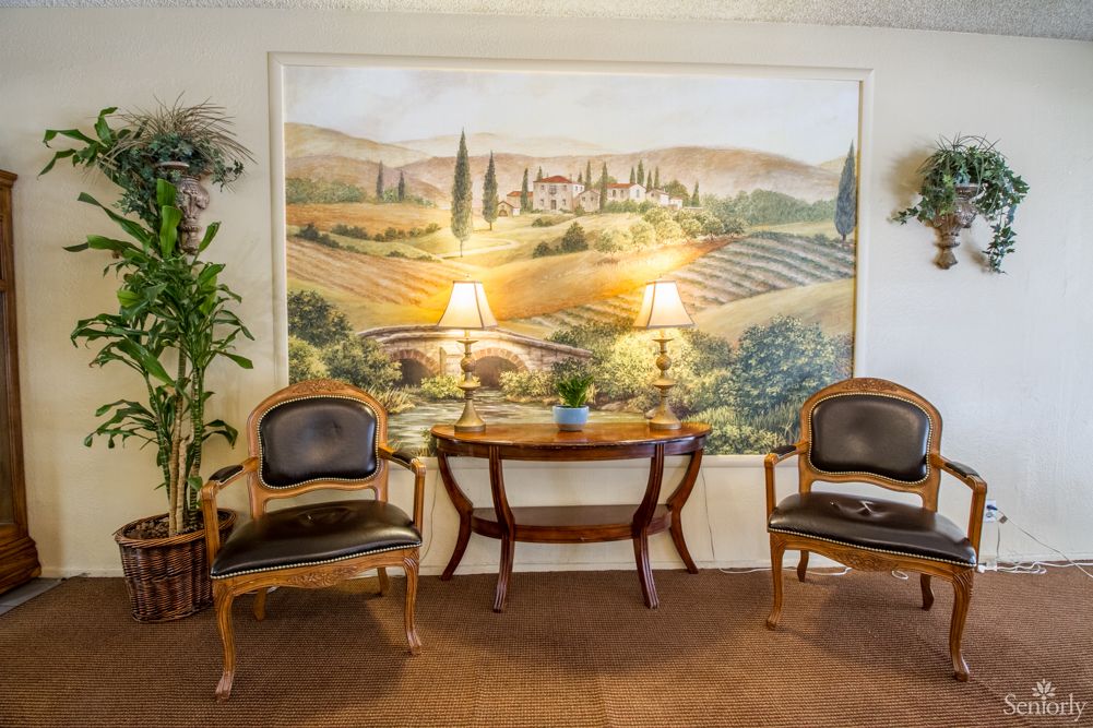A cozy seating area featuring two chairs and a table, flanked by lamps, with a mural of a scenic landscape in the background.