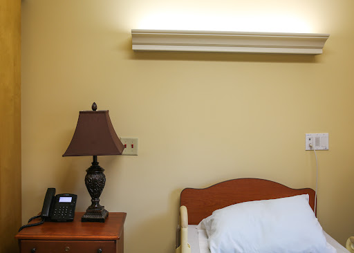 A cozy bedroom corner featuring a bed, a lamp on a nightstand, and soft lighting.
