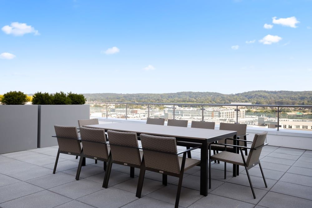 A spacious outdoor patio with a large table and chairs, offering a scenic view of hills under a clear blue sky.