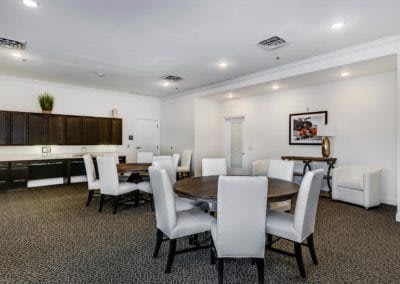 Spacious dining area with round tables and white upholstered chairs, featuring a kitchenette and contemporary artwork.