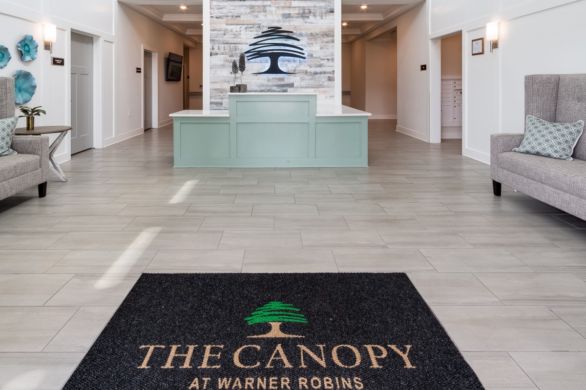 A modern lobby with a welcome mat featuring the logo 'The Canopy at Warner Robins'.