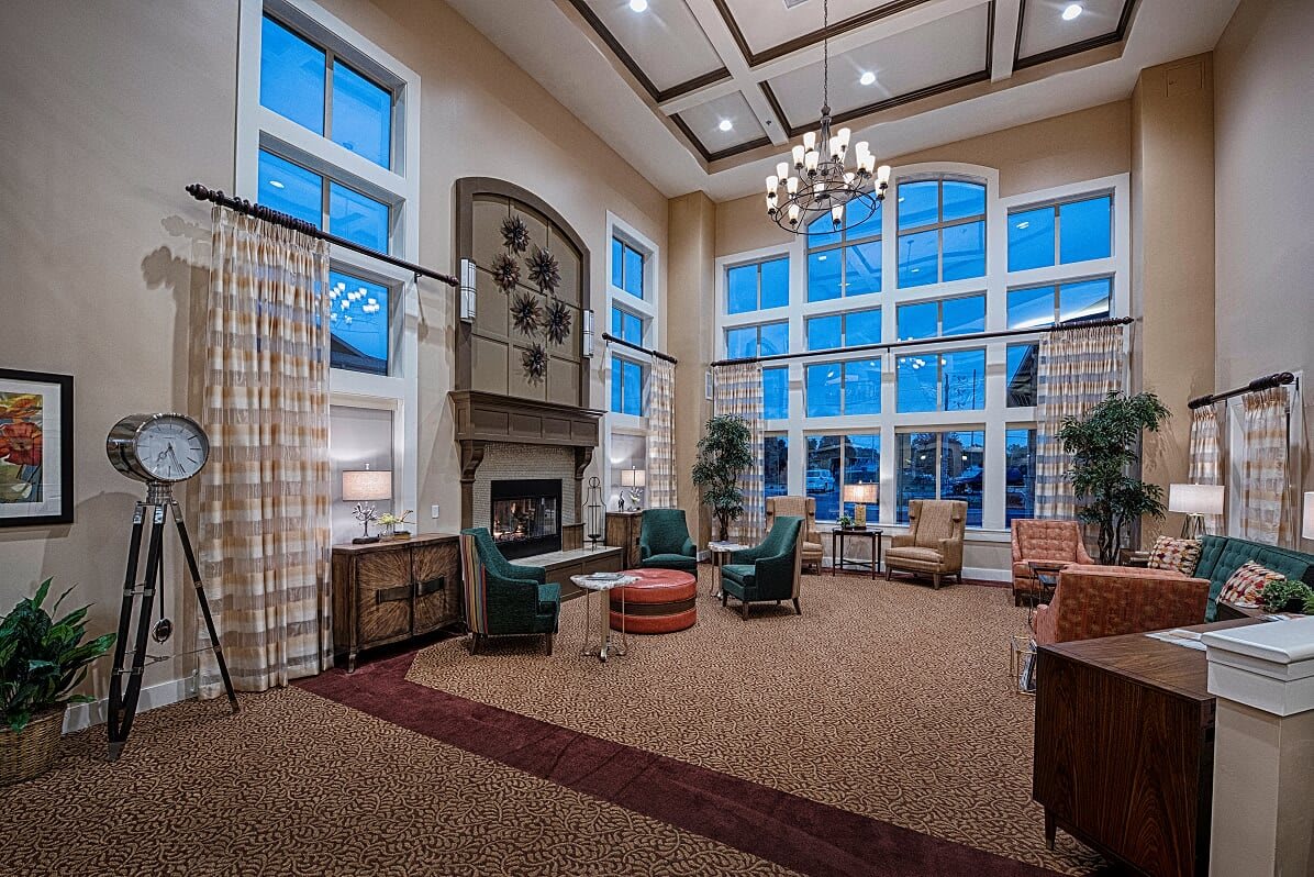 A spacious living room with a high ceiling, featuring a fireplace, comfortable seating, and large windows that let in ample natural light.