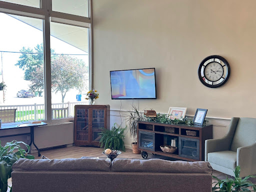 A cozy living room with a modern aesthetic, featuring a television and decorative plants near large windows.