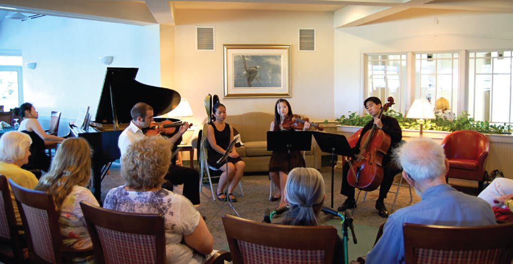 A chamber music group performs for an intimate audience in a cozy indoor setting.