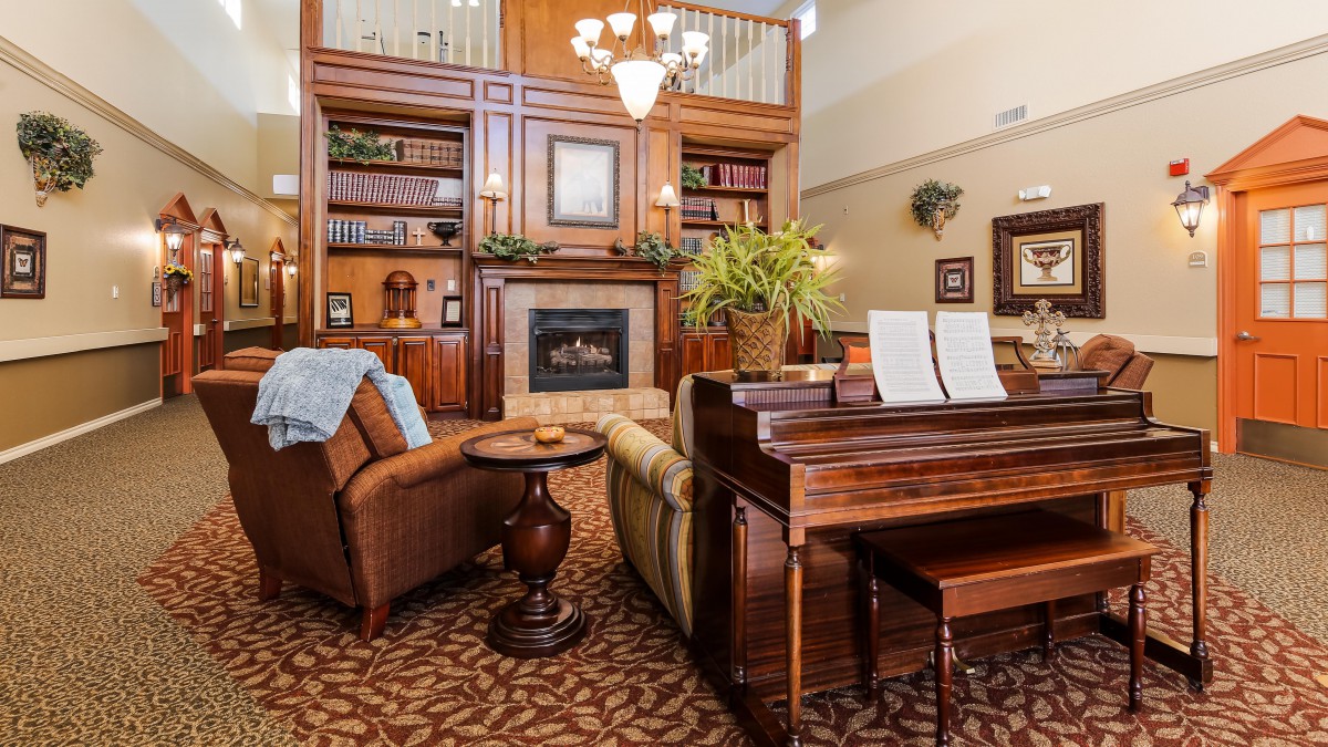 A cozy living room with a fireplace and piano, surrounded by bookshelves and elegant decor.