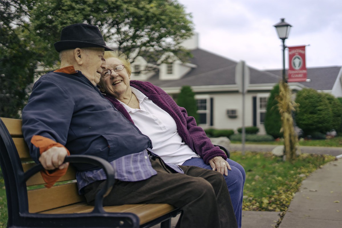 An elderly couple shares a moment of affection while sitting on a park bench.