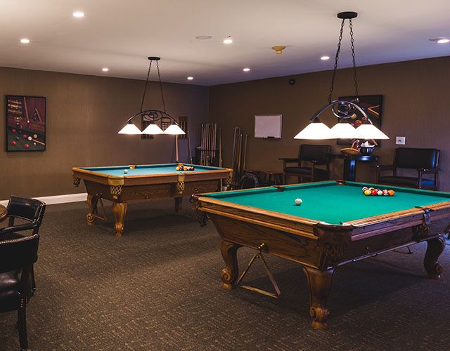 A cozy game room featuring two pool tables under hanging lights.