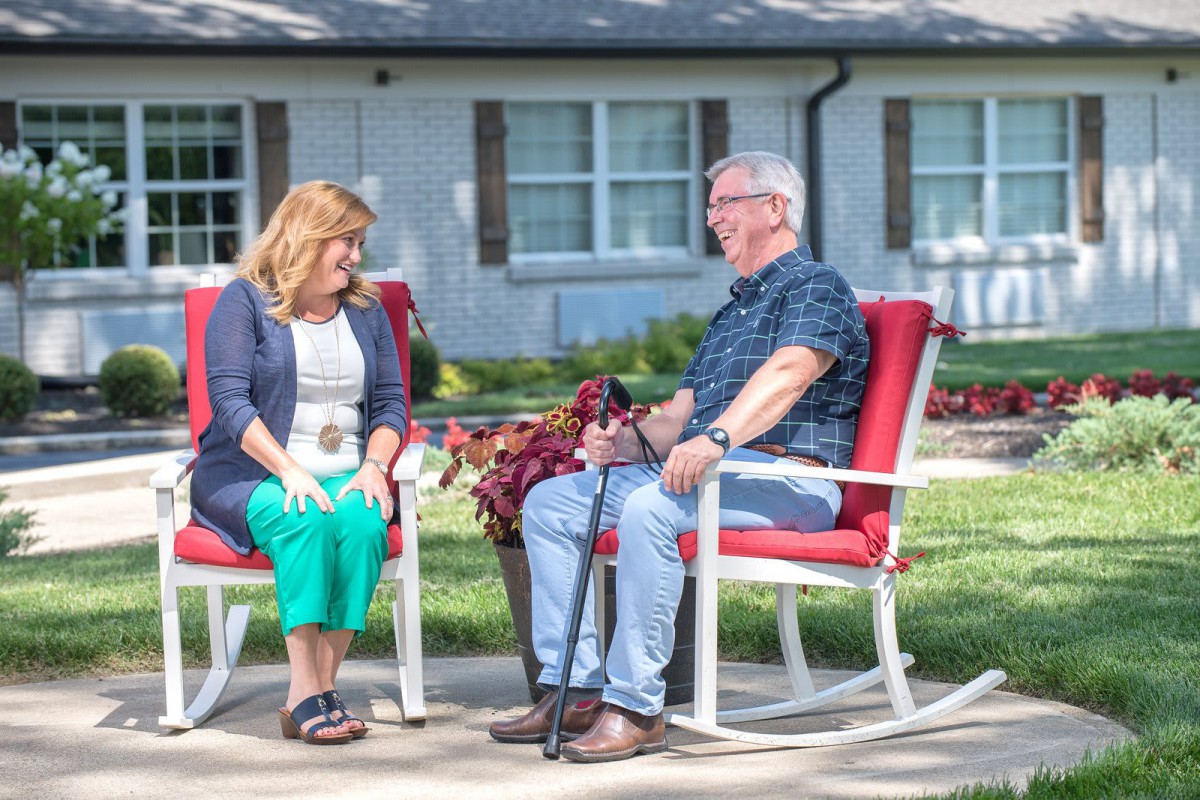 Two people sitting on red chairs having a conversation in a garden setting.