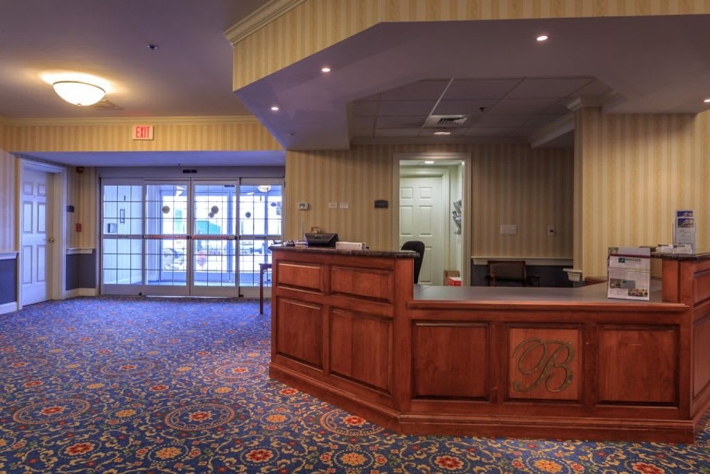 A hotel lobby with a wooden reception desk and colorful carpet.