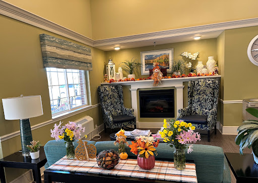 A cozy living room adorned with autumn decorations and fresh flowers, featuring comfortable seating by the fireplace.