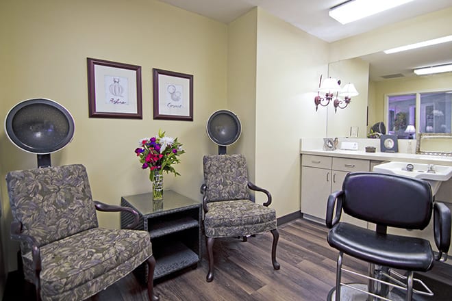 A cozy salon waiting area with chairs, a hair dryer, and a floral arrangement.