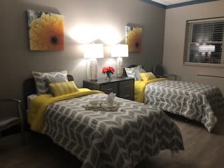 A cozy bedroom with two twin beds featuring yellow and gray decor, highlighted by floral artwork above the headboards.