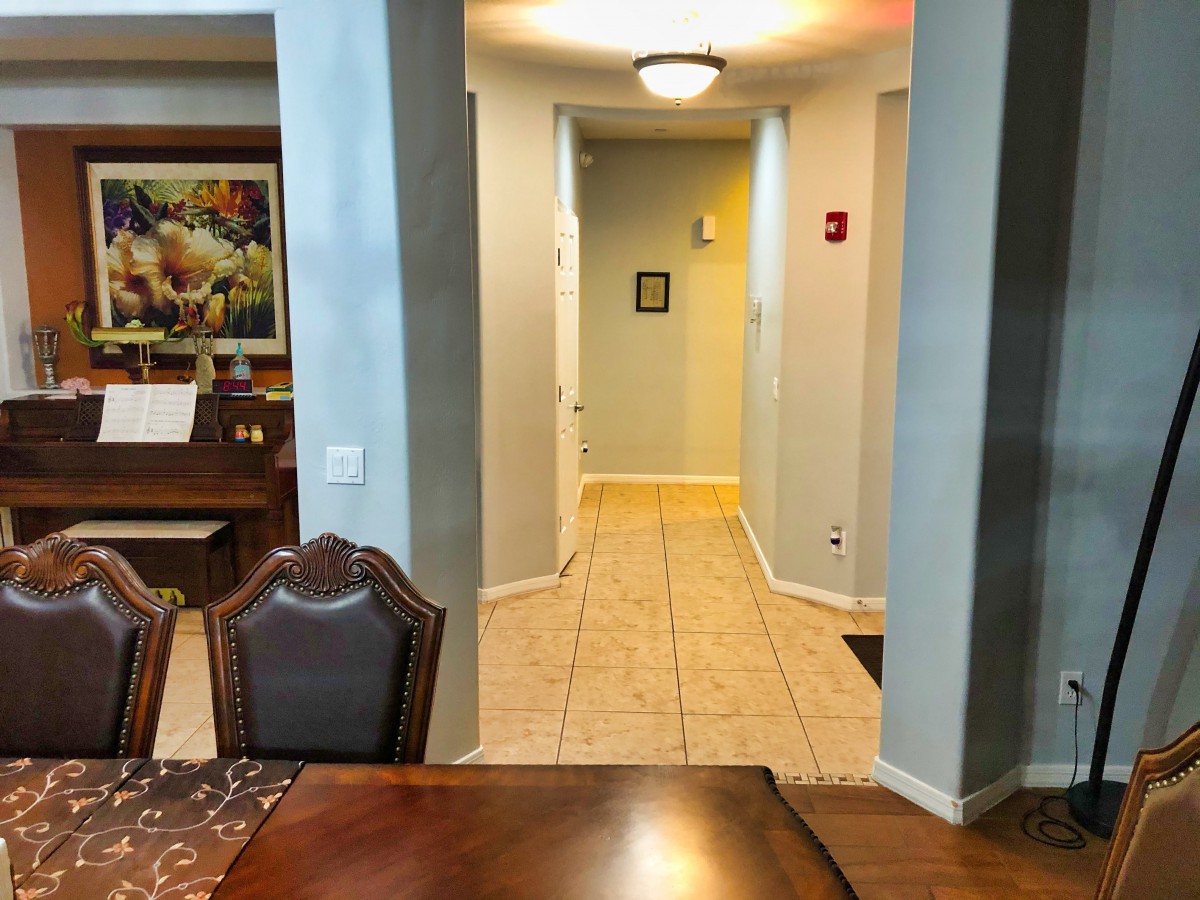A view from a dining room into a hallway, featuring tiled floors and artwork on the wall.