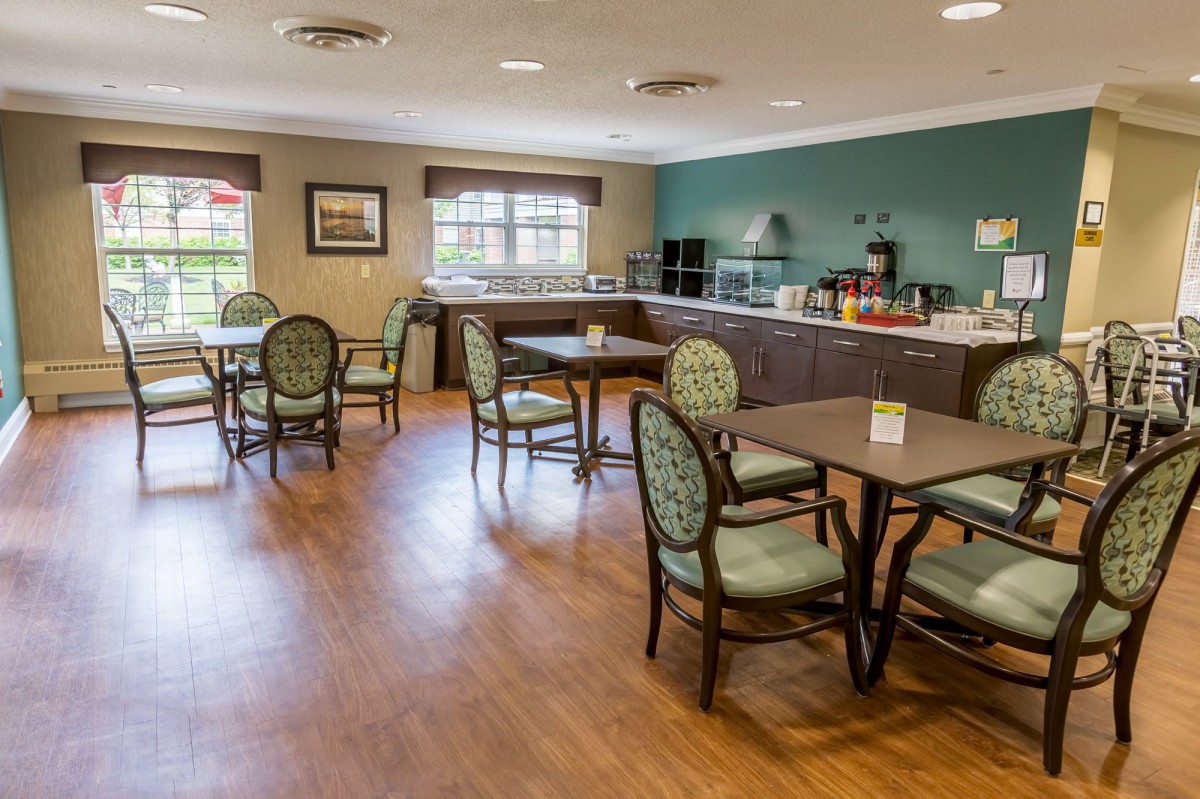A cozy dining area with tables and chairs arranged in a cafe-style setting, featuring bright lighting and wooden flooring.